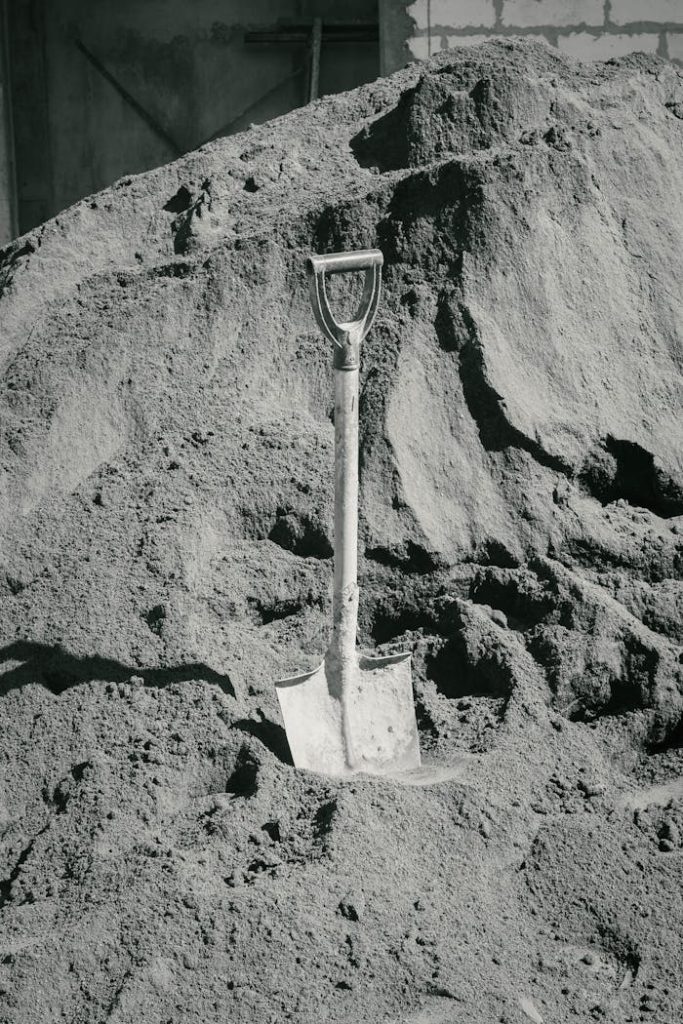 A solitary shovel upright in a massive sand pile, representing construction and labor.